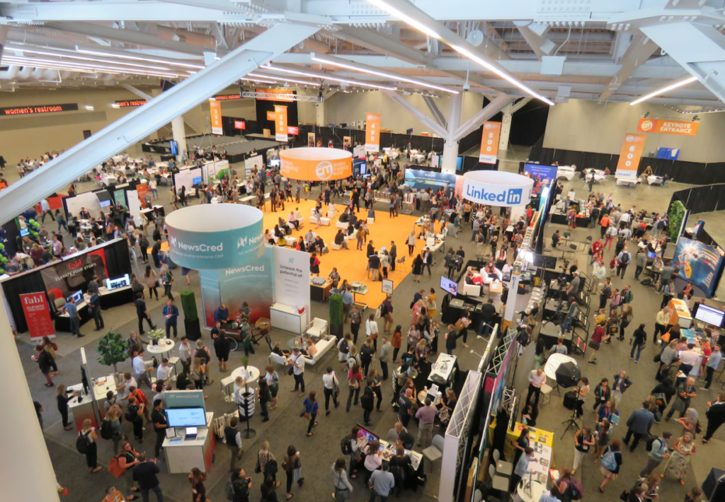 Large expo hall at Content Marketing World with attendees walking between exhibitor booths, networking areas, and branded displays