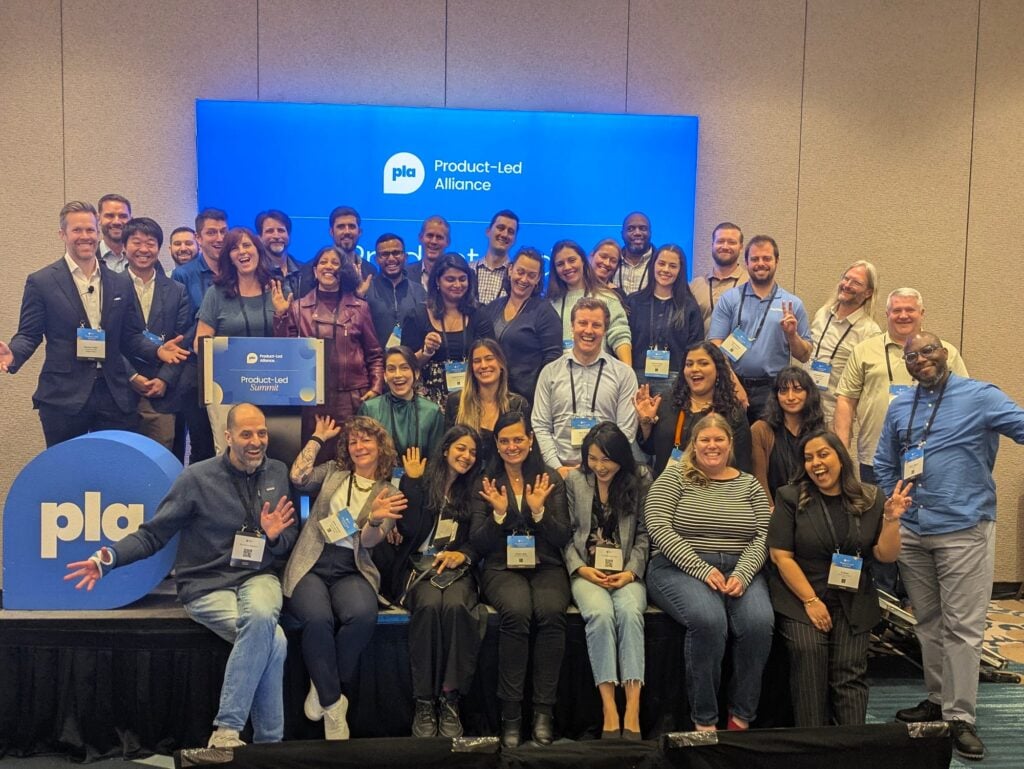 Grupo de asistentes posando en el Product-Led Summit con la marca Product-Led Alliance al fondo.